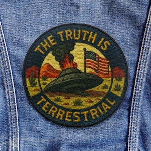 Può includere: Una toppa rotonda con la scritta "THE TRUTH IS TERRESTRIAL" che circonda una scena con un UFO, la bandiera americana e un paesaggio desertico. La toppa è principalmente blu navy, con dettagli gialli, rossi e verdi, cucita su una giacca di jeans.