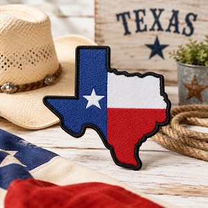 May include: A Texas-shaped patch with the state flag design: blue with a white star, white, and red. The patch is on a white wooden surface, with a cowboy hat, rope, and a wooden sign that says "TEXAS" in the background.
