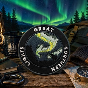 May include: A circular embroidered patch featuring a dark blue night sky with a vibrant green aurora borealis and a black silhouette of a forest. The text GREAT NORTHERN LIGHTS is stitched in white capital letters along the black border.