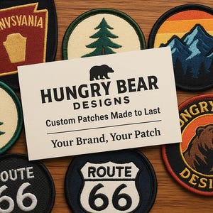 May include: A collection of embroidered patches with various designs, including a Pennsylvania state patch, a Route 66 patch, and patches featuring mountains and trees. A card reads "HUNGRY BEAR DESIGNS, Custom Patches Made to Last."