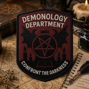 May include: A shield-shaped embroidered patch featuring the text DEMONOLOGY DEPARTMENT and CONFRONT THE DARKNESS in white. The design includes a red pentagram, black bat wings, and silhouettes of candles and an open book on a dark red background.
