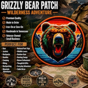 Peut inclure: Un écusson brodé circulaire représentant une tête d'ours grizzly gueule ouverte, sur un fond composé d'eau bleue, d'arbres verts, de montagnes blanches et d'un ciel au coucher du soleil avec des bandes horizontales orange, rouge et jaune.