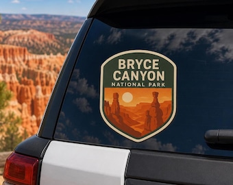 Könnte beinhalten: Ein schildförmiger Aufkleber auf einer Fahrzeugscheibe mit dem Text BRYCE CANYON NATIONAL PARK in cremefarbenen Buchstaben. Das Design zeigt eine stilisierte orange- und braunfarbene Canyon-Landschaft mit Felsnadeln unter einer blassen Sonne.