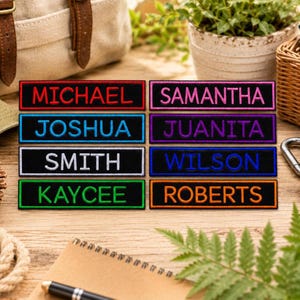 May include: A collection of embroidered name patches in various colors. Each patch features a different name in a contrasting color, including "MICHAEL," "SAMANTHA," "JOSHUA," "JUANITA," "SMITH," "WILSON," "KAYCEE," and "ROBERTS."