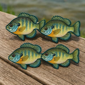 May include: Four embroidered fish patches. Each patch features a blue, yellow, and orange fish with detailed stitching. The patches are arranged on a wooden surface, showcasing the intricate design and vibrant colors of the aquatic creatures.
