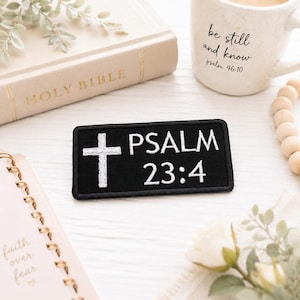 Pode incluir: Um patch retangular preto com uma cruz branca e o texto "PSALM 23:4". A imagem inclui uma Bíblia, uma caneca com a frase "be still and know", um caderno e elementos decorativos.