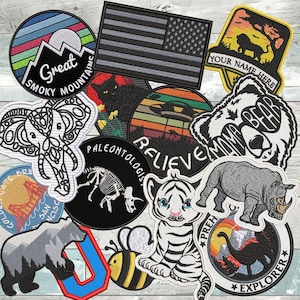 May include: A collection of embroidered patches with various designs. Includes a gray American flag, a bear with "BEAR MAMA" text, a tiger cub, a rhino, and a patch with "Great Smoky Mountains" text.