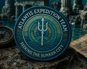 Peut inclure: Un écusson rond bleu et vert avec le texte "ATLANTIS EXPEDITION TEAM" et "SEEKING THE SUNKEN CITY". Il présente un trident et des vagues stylisées, évoquant un thème sous-marin. Une boussole et une carte sont en arrière-plan.
