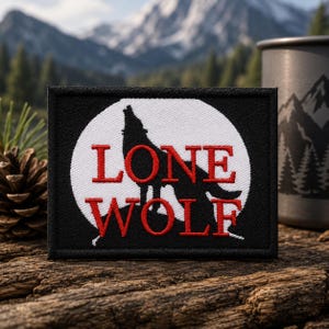Puede incluir: Un parche bordado rectangular con borde negro y fondo circular blanco. Una silueta negra de un lobo aullando está centrada dentro del círculo. El texto bordado en rojo LONE WOLF está posicionado sobre la silueta del lobo.