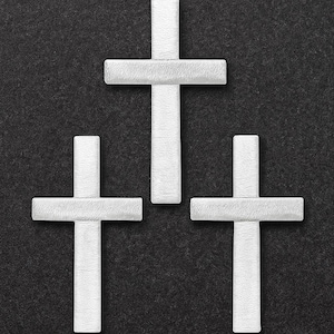 Może przedstawiać: Trzy białe krzyże ułożone na ciemnym, teksturowanym tle. Krzyże mają prosty, prostokątny kształt. Obraz jest widokiem z góry, z równomiernie rozmieszczonymi krzyżami.