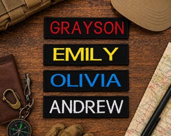 Könnte beinhalten: Vier rechteckige, schwarze bestickte Aufnäher mit den Namen GRAYSON in Rot, EMILY in Gelb, OLIVIA in Blau und ANDREW in Weiß. Jeder Aufnäher hat einen sauber vernähten Rand und eine zentrierte, großgeschriebene Beschriftung.