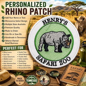 May include: A circular embroidered patch featuring a grey rhinoceros illustration on a light green background, enclosed by a white border. The text 'HENRY'S' is arched at the top and 'SAFARI ZOO' is arched at the bottom in black lettering.