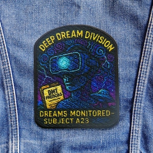 以下が含まれることがあります： 黄色で「DEEP DREAM DIVISION」の文字とVRゴーグルをかけた人のグラフィックが描かれた黒いパッチ。パッチには「DREAMS MONITORED - SUBJECT A23」と「DMT PROTOCOLS」の文字も含まれています。デザインは青、紫、黄色の色合いです。