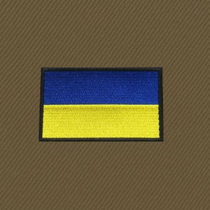 May include: Embroidered patch featuring the Ukrainian flag, a horizontal bicolor of blue and yellow. The patch has a black border and is set against a brown, textured background. The flag design is neatly stitched.