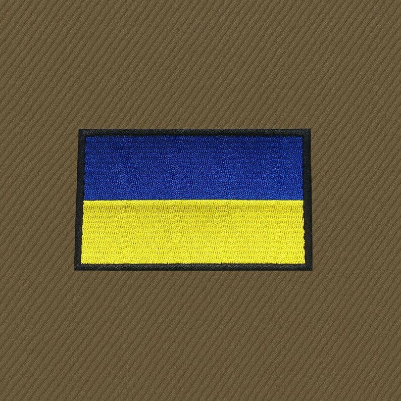 May include: Embroidered patch featuring the Ukrainian flag, a horizontal bicolor of blue and yellow. The patch has a black border and is set against a brown, textured background. The flag design is neatly stitched.