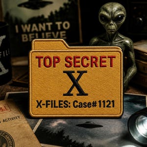 May include: A yellow patch with the text "TOP SECRET X-FILES: Case#1121" in red and black. The patch is on a table with an alien figurine, a torch, and a mug with the X-Files logo. A sign that says "I WANT TO BELIEVE" is in the background.