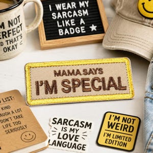 May include: A rectangular embroidered patch with a tan background and a metallic gold border. The text MAMA SAYS I'M SPECIAL is stitched in dark brown thread across the center. The patch is positioned among other items with text-based designs.