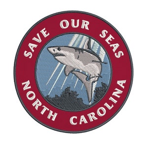 May include: Embroidered patch with a shark leaping from the ocean. The patch is circular with a red border and the text "SAVE OUR SEAS NORTH CAROLINA" in white. The shark is gray and white.