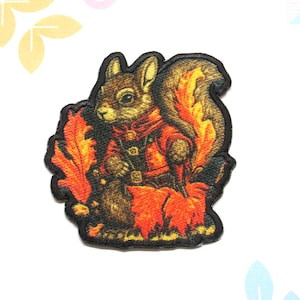 May include: A brown squirrel wearing a red and gold jacket sits on a bed of orange and yellow leaves. The squirrel's tail is curled up behind it. The image is a patch with a black border.