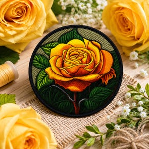 May include: A circular embroidered patch featuring a vibrant yellow and orange rose with deep green leaves. The rose is centered within the black-bordered circle, showcasing intricate thread work that captures the layered petals and foliage.