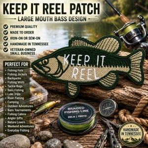 Può includere: Una toppa ricamata a forma di pesce con una combinazione di colori verde scuro e beige e la scritta bianca KEEP IT REEL cucita al centro. La toppa è mostrata insieme a varie attrezzature da pesca, tra cui un mulinello, lenza e bussola.
