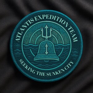 May include: A round, teal patch with the text "ATLANTIS EXPEDITION TEAM" and "SEEKING THE SUNKEN CITY" in white lettering. The patch features a trident, bell, and waves design.