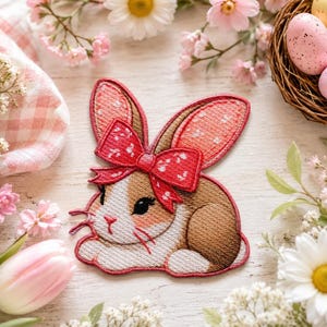 May include: An embroidered bunny patch with a red bow and pink polka dots on its ears. The bunny is brown and white, with a red outline. The patch is surrounded by flowers and Easter eggs.