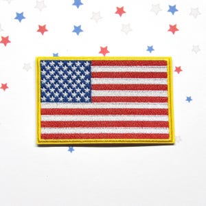 May include: A rectangular embroidered patch featuring the United States flag with a blue canton containing white stars and alternating red and white horizontal stripes. The entire flag design is bordered by a thick, solid yellow stitched edge.