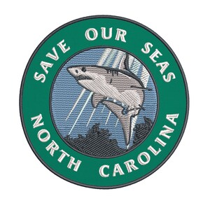 May include: Embroidered patch with a green border and the words "SAVE OUR SEAS NORTH CAROLINA". The patch features a shark leaping out of the water with a blue and white background.