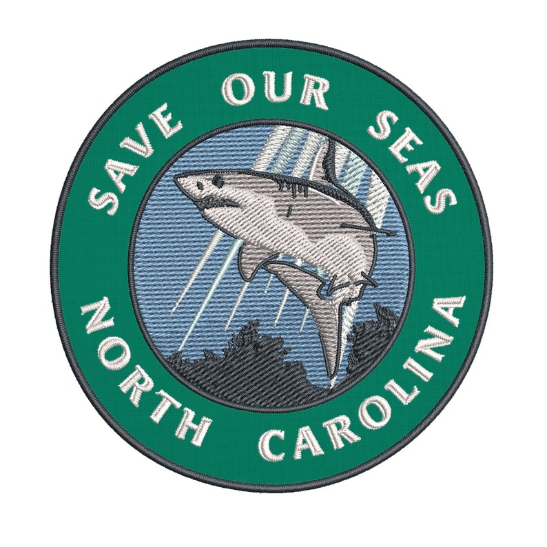 May include: Embroidered patch with a green border and the words "SAVE OUR SEAS NORTH CAROLINA". The patch features a shark leaping out of the water with a blue and white background.