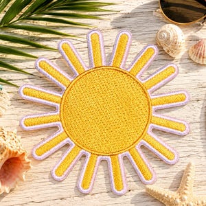 Puede incluir: Un parche bordado circular que presenta un sol amarillo brillante con un centro texturizado y rayos radiantes. El sol est&aacute; delineado con un borde de color lavanda claro, creando un contraste distintivo con la tela amarilla del dise&ntilde;o.