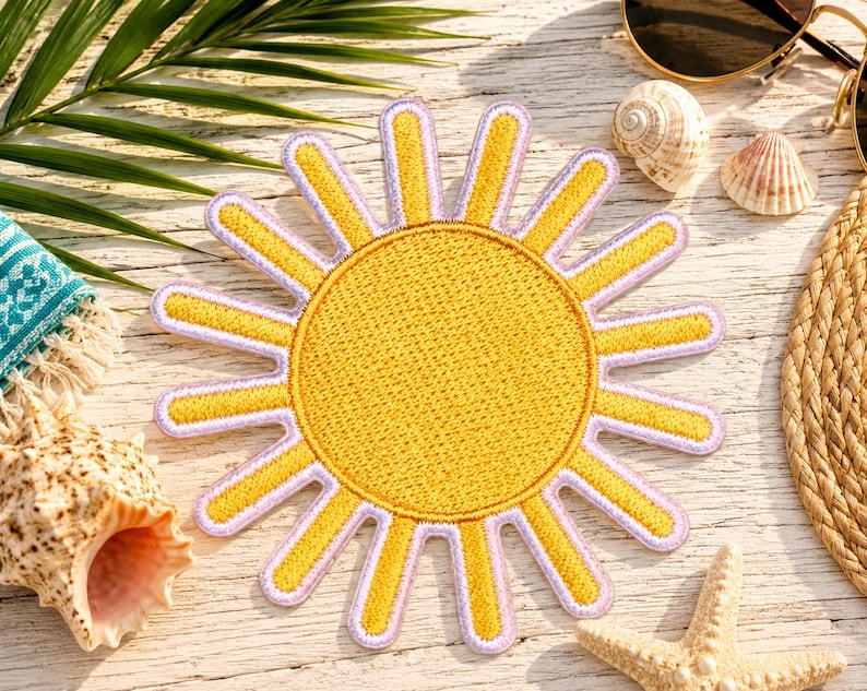 Puede incluir: Un parche bordado circular que presenta un sol amarillo brillante con un centro texturizado y rayos radiantes. El sol est&aacute; delineado con un borde de color lavanda claro, creando un contraste distintivo con la tela amarilla del dise&ntilde;o.