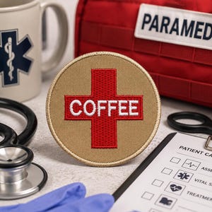 Puede incluir: Un parche circular de color tostado con una cruz roja y el texto blanco COFFEE bordado en el centro. El parche está colocado entre equipo médico que incluye un estetoscopio, un portapapeles de informe de paciente y un bolso paramédico rojo.
