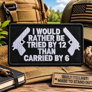 May include: Black rectangular patch with white embroidered text: "I WOULD RATHER BE TRIED BY 12 THAN CARRIED BY 6." Features white gun outlines. A smaller patch reads "BUILT TO LAST. MADE TO STAND OUT." Other items in the background.