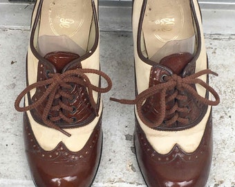 May include: A pair of brown and white leather shoes with lace-up fastenings. The shoes feature a wingtip design and a glossy finish.