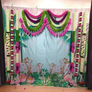 May include: A decorative backdrop for a special event, featuring a blue and green floral design with white cows. The backdrop is adorned with garlands of white, green, and pink flowers.