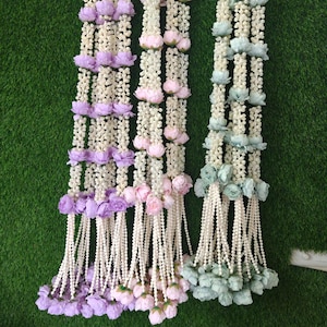 May include: Three decorative floral garlands in shades of purple, pink, and green. Each garland features white beaded strands with clusters of flowers and hanging beaded tassels. The garlands are displayed against a green background.