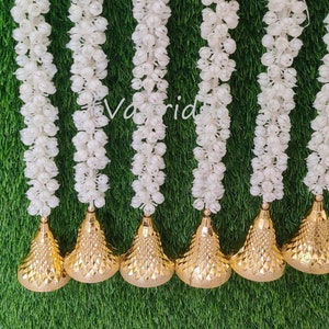 May include: Six white flower garlands with gold-colored cone-shaped accents hanging against a green background.