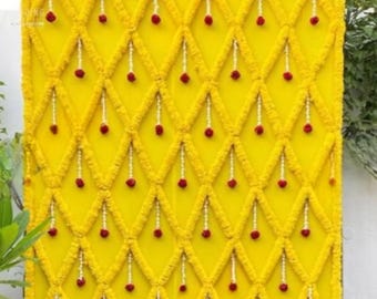 May include: A yellow backdrop decorated with red flowers and white garlands. The flowers and garlands are arranged in a diamond pattern.