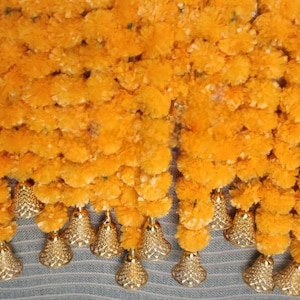 May include: A garland of yellow fabric flowers with gold bells hanging from the bottom. The garland is made of many small, fluffy flowers.
