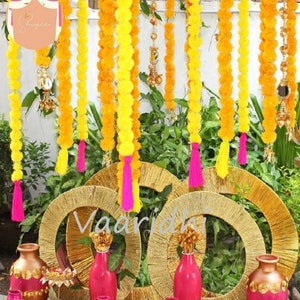 Pode incluir: Um cenário de cerimônia de casamento decorado com guirlandas de flores de calêndula amarelas, borlas rosa e coroas circulares douradas. O cenário é adornado com vasos cheios de flores rosa e detalhes dourados.