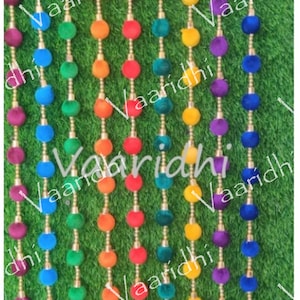 Pode incluir: Uma guirlanda colorida de pompons, com cada fio de uma cor diferente. A guirlanda é feita de vários fios de pompons, cada fio de uma cor diferente, incluindo azul, verde, amarelo, laranja e vermelho.