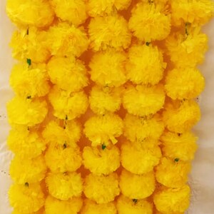 May include: A garland of yellow marigold flowers, strung together with green stems. The garland is made of artificial flowers and is perfect for decorating for a special occasion.