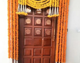 May include: A wooden door decorated with garlands of orange and yellow marigold flowers. The garlands are strung together with white beads and hang on either side of the door.