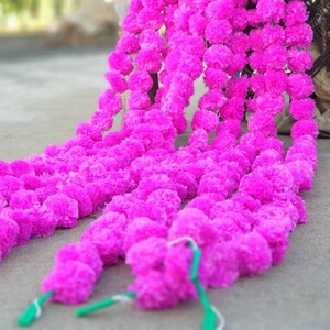 May include: A long garland of pink paper flowers, strung together in a continuous line. The garland is made of multiple strands of flowers, creating a full and lush look.