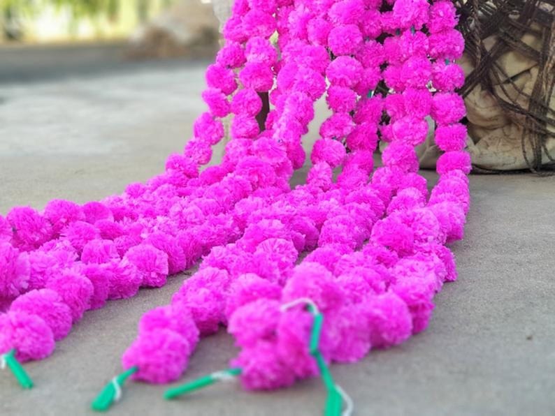 May include: A long garland of pink paper flowers, strung together in a continuous line. The garland is made of multiple strands of flowers, creating a full and lush look.