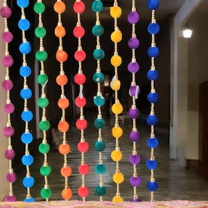 May include: A colorful beaded curtain with a rainbow of plush, round ornaments. The beads are strung vertically with gold-colored connectors, creating a vibrant and decorative doorway accent. The colors include purple, blue, green, orange, and red.