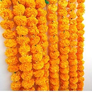 May include: A garland of bright yellow marigold flowers, strung together in a long strand. The garland is made of artificial flowers and is perfect for decorating for a special occasion.