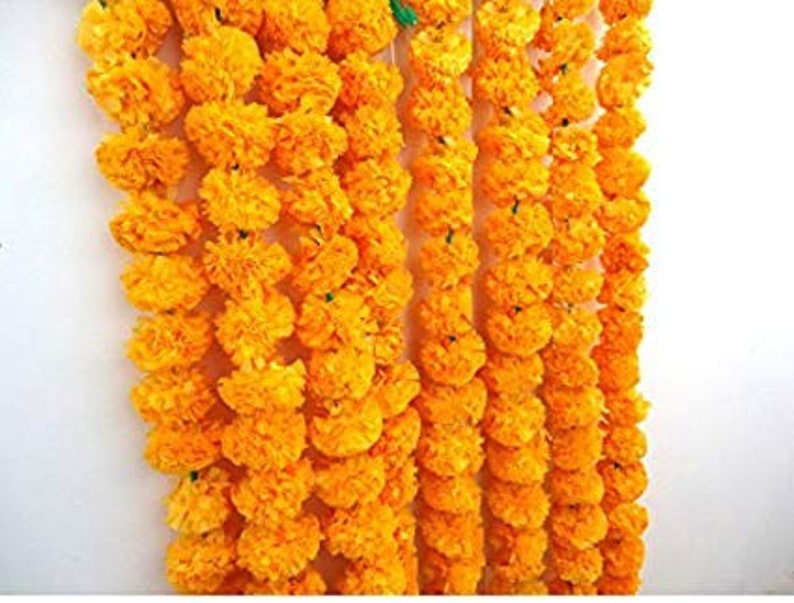 May include: A garland of bright yellow marigold flowers, strung together in a long strand. The garland is made of artificial flowers and is perfect for decorating for a special occasion.