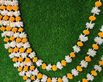 May include: Close-up of decorative garlands with alternating white and orange floral elements. The garlands are arranged against a green background, creating a vibrant contrast. The floral design is detailed and symmetrical, suggesting a handcrafted or traditional style.